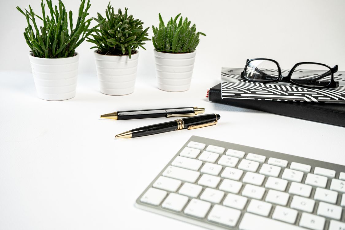Modern workspace with a keyboard, pens and notebooks on a clean white desk