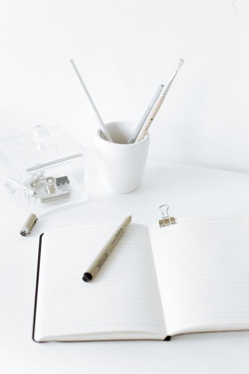 An open notebook with a pen on a minimalist white desk