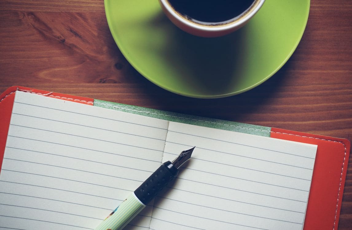 Elegant fountain pen resting on an open notebook beside a warm coffee mug on a wooden desk