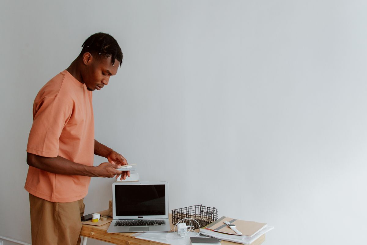 Man organising his workspace at a standing desk with a laptop and office supplies