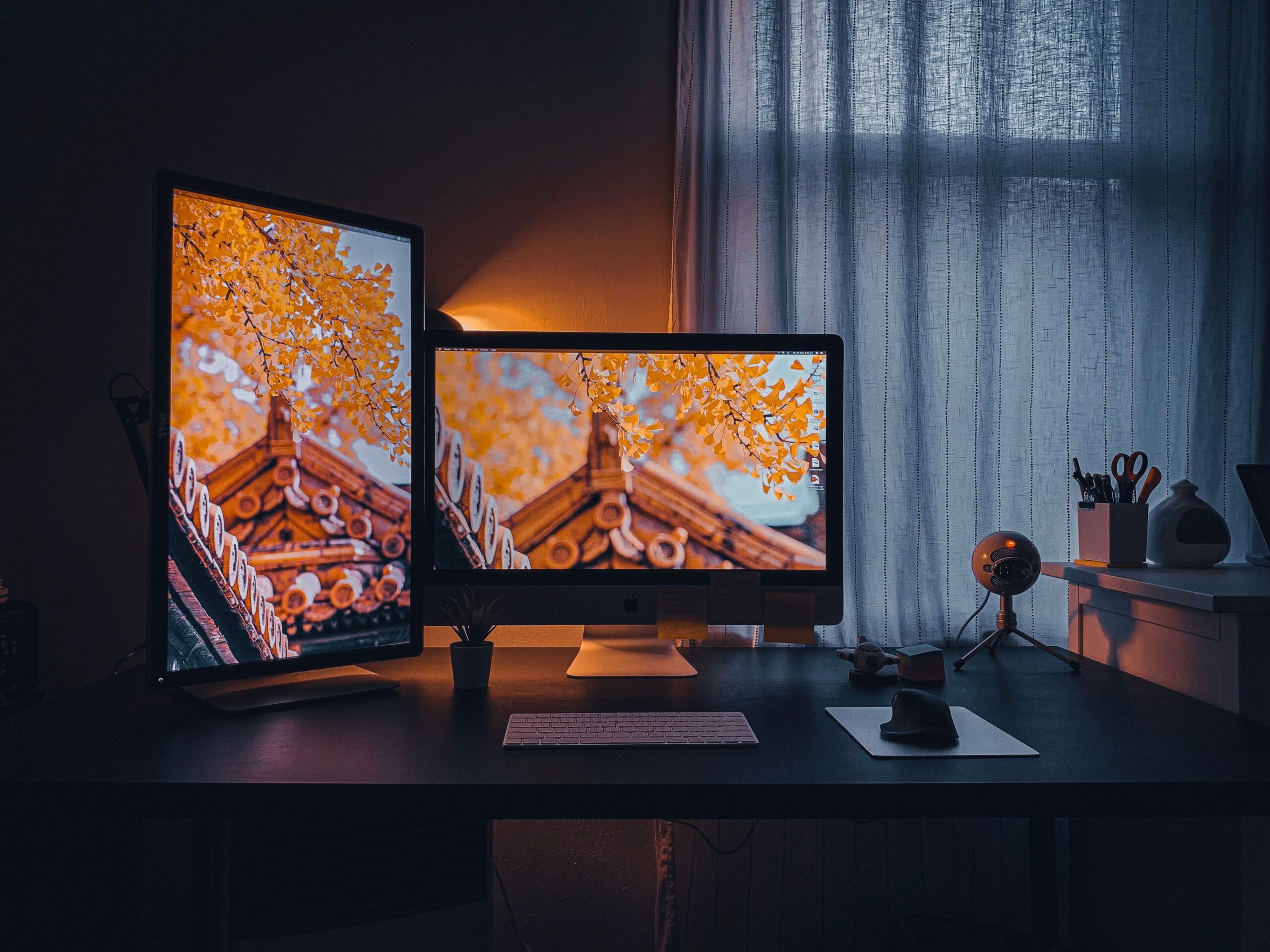 A cozy home office desk with dual monitors, keyboard and warm ambient lighting