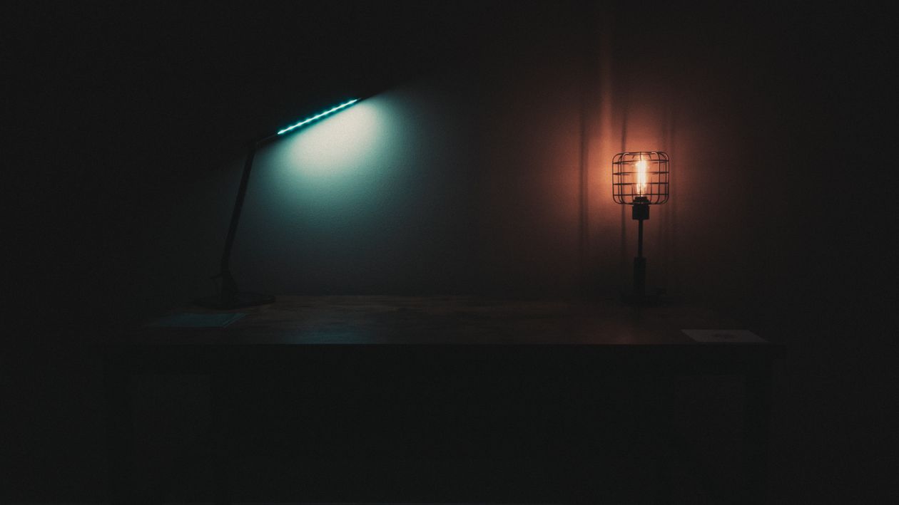 Desk lamps casting warm and cool light in a dark home office, showing lighting contrast